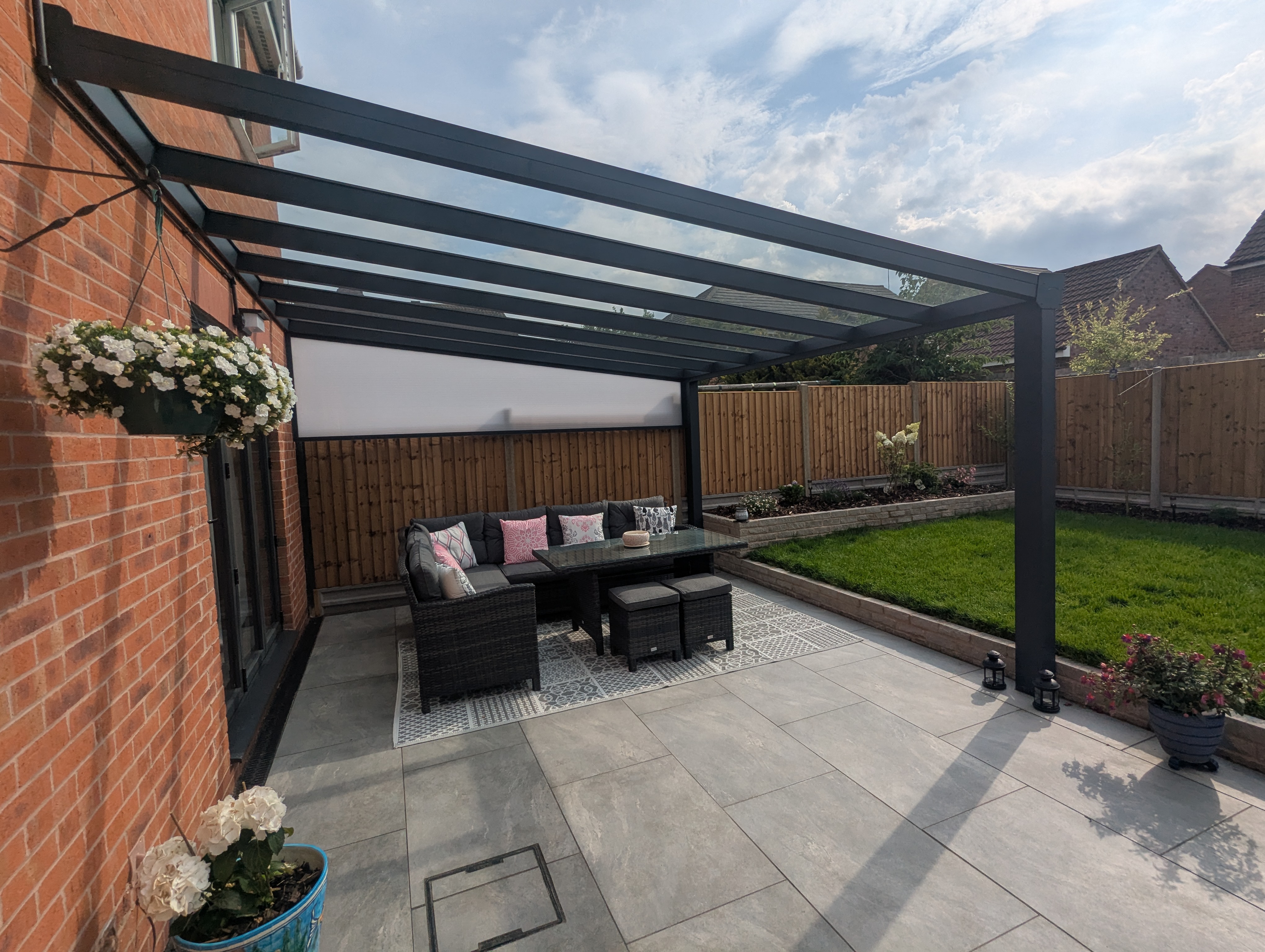 Anthracite aluminium veranda over a stone-paved patio with corner sofa, brick home behind