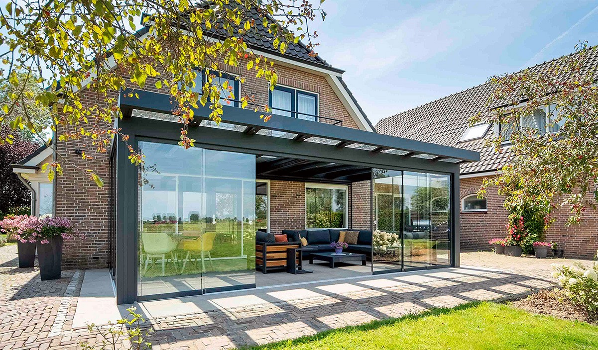 A glass-roofed veranda set against a Dutch-style home in autumn