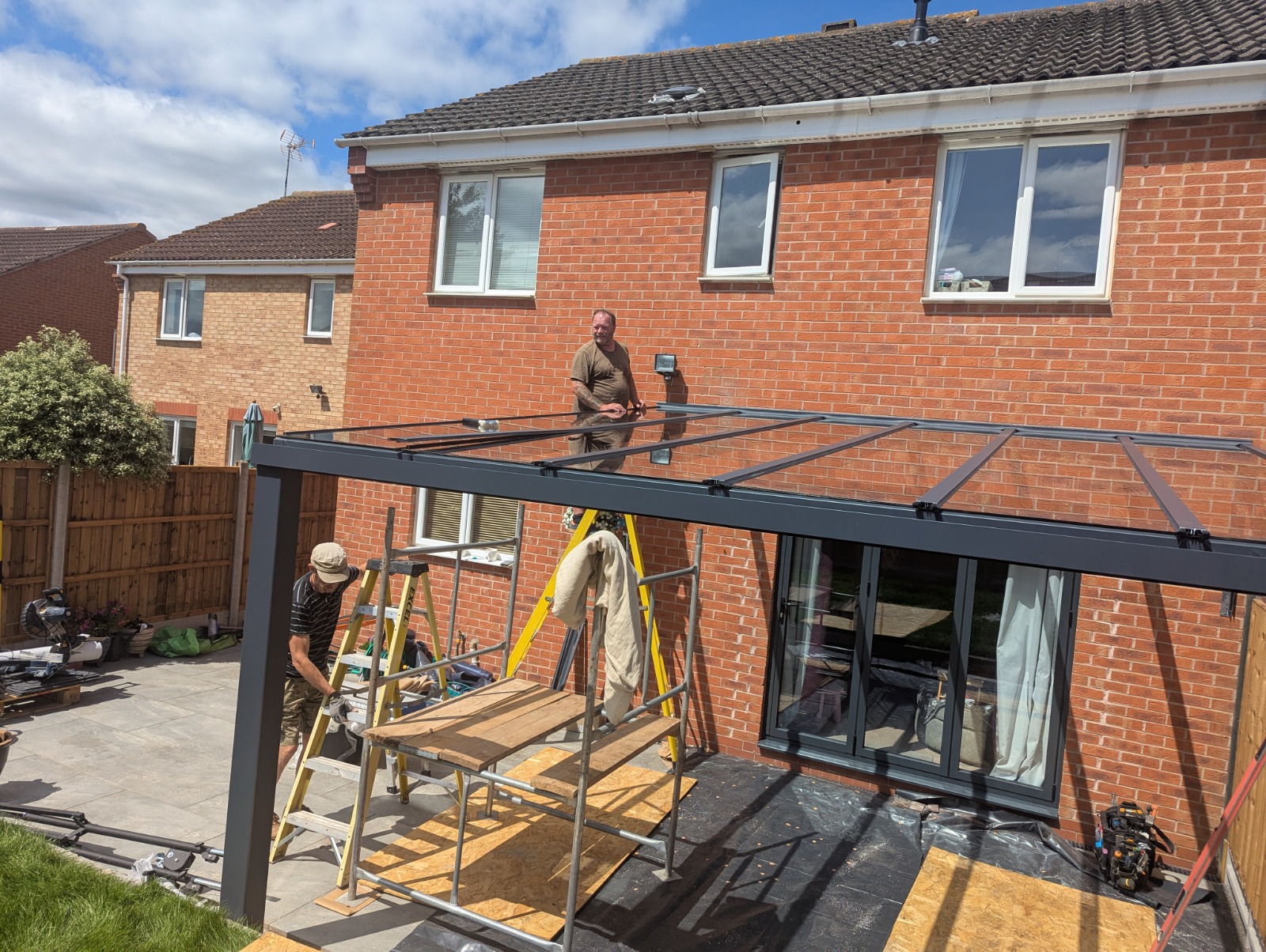 Two installers building an aluminium veranda frame at the rear of a brick home