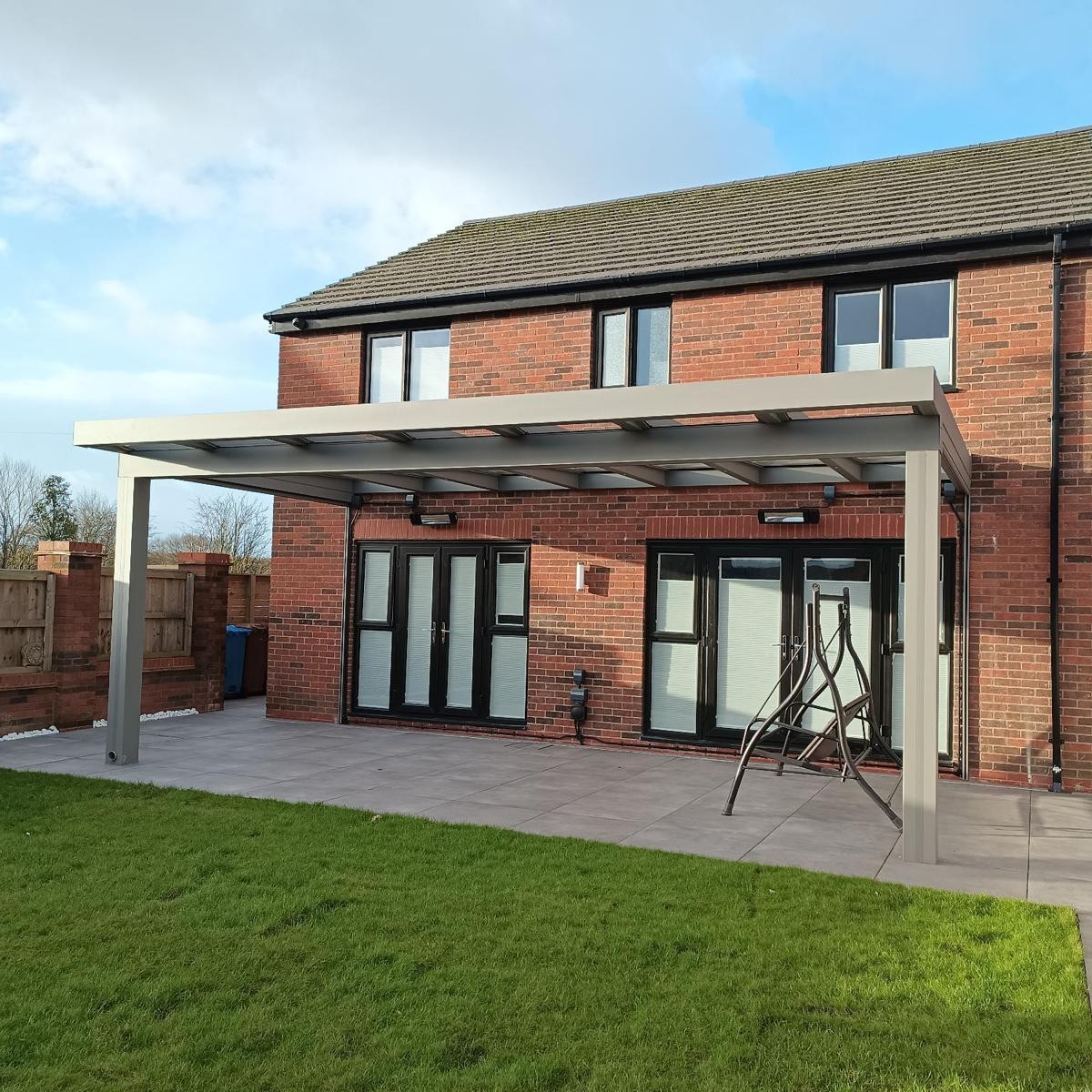 Silver-bronze CubeLine aluminium veranda with a glass roof over a paved patio