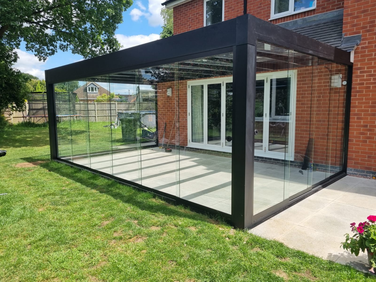 A fully enclosed glass garden room with anthracite frame, set against a modern white house